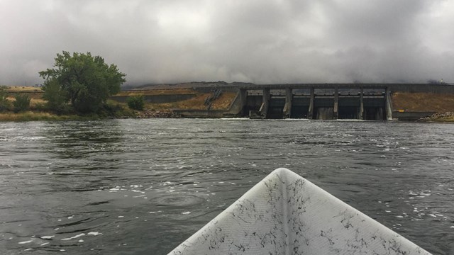 Bow of a boat pointed at a dam on a river