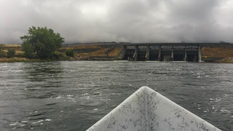 Bow of a boat pointed at a dam on a river
