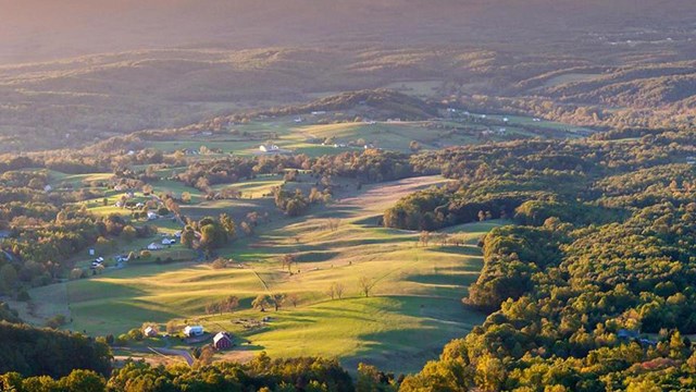 Aerial view of lush valley and wooded area at sunset, mountains in distance