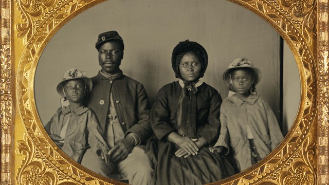 A black soldier and his wife and two children sit for a photo