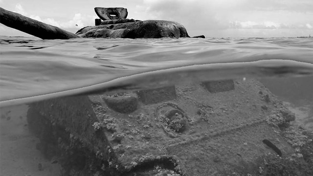 Metal tanker vehicle half submerged in ocean, covered in barnacles