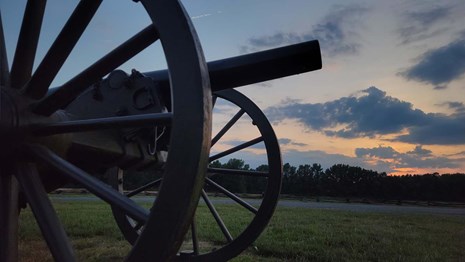 Morning light peaks through clouds over field, closeup of cannon in foreground