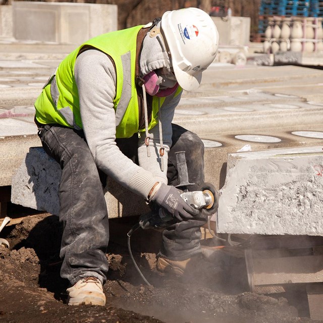 Person in hardhat and safety vest grinds large marble stone