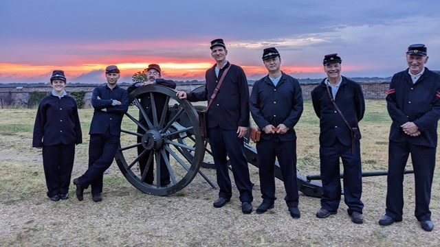 A group of people standing by a canyon at sunset.