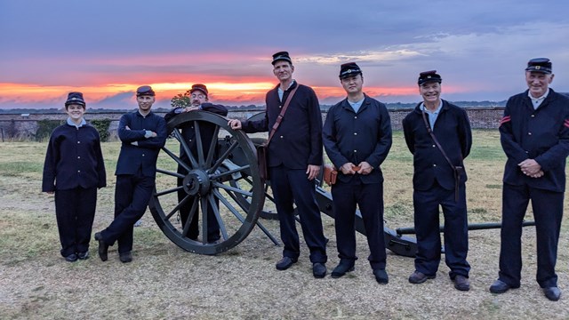 A group of people standing by a cannon at sunset.