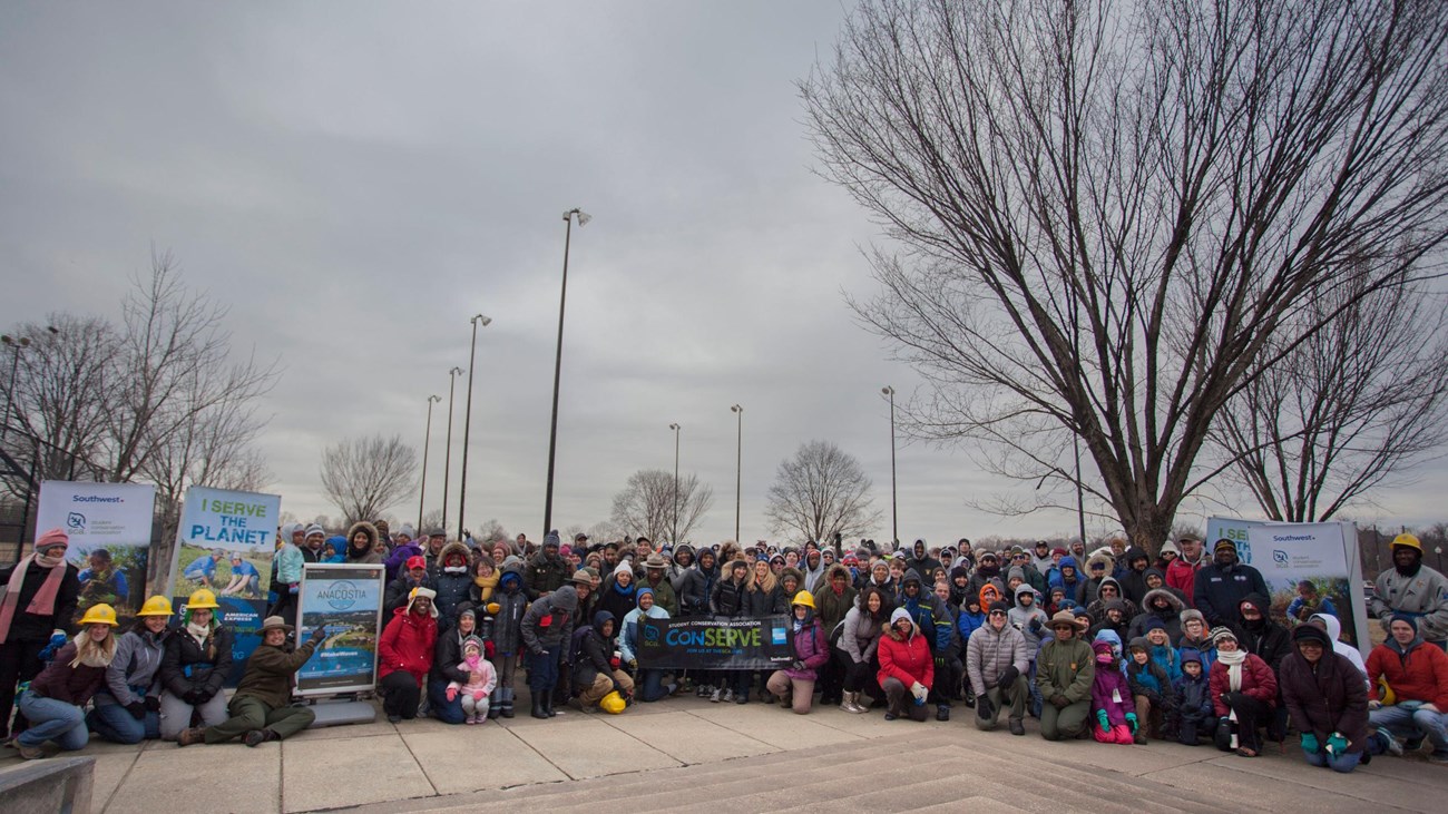 A large group of people standing on concrete in front of trees.