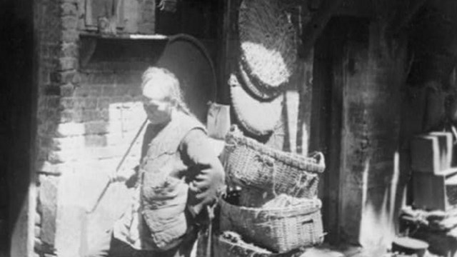 A man smokes a long pipe in Rag Pickers Alley in Chinatown, San Francisco. Photo, ca. 1921