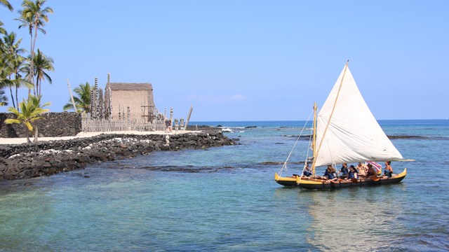 A double-hulled canoe approaching a Hawai'ian temple on a coast