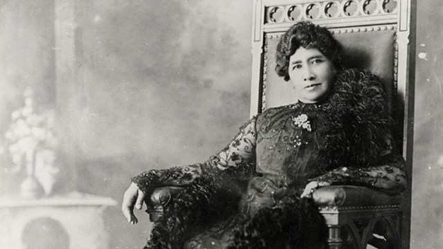 Black and white photo of Queen Liliuokalani in 1900, sitting on a throne in royal garments.