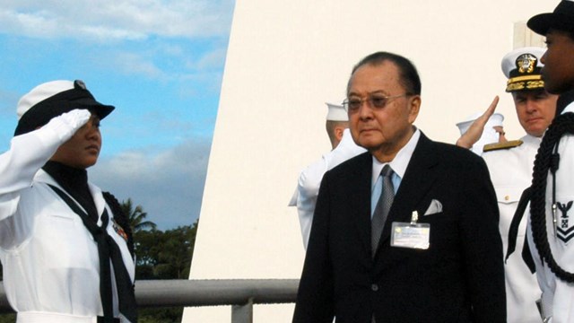 Color photo of US Senator Daniel Inouye at the USS Arizona Memorial, saluted by Navy shipmen.