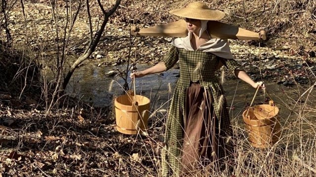 woman in an1800s dress carrying water