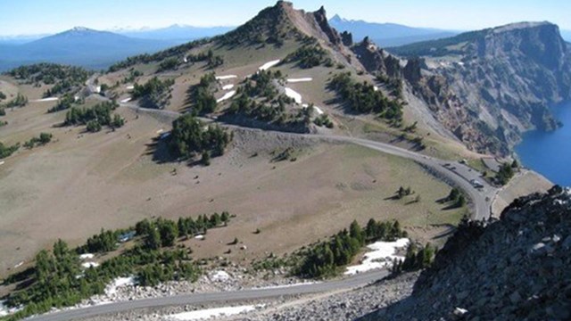 a road winds along a hill crest beside the cliffs of a deep blue lake