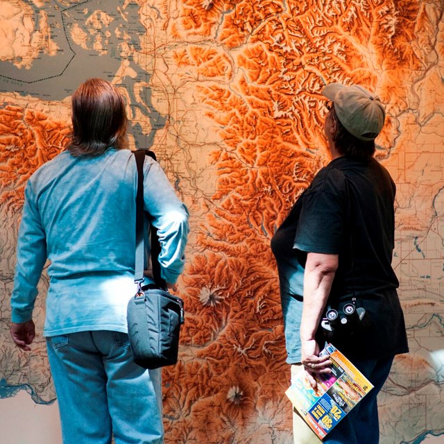 Two visitors looking at a tall wall map of a park