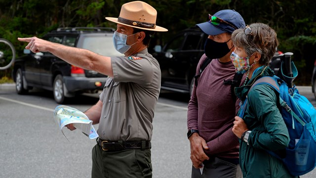 a man in uniform points as visitors look on