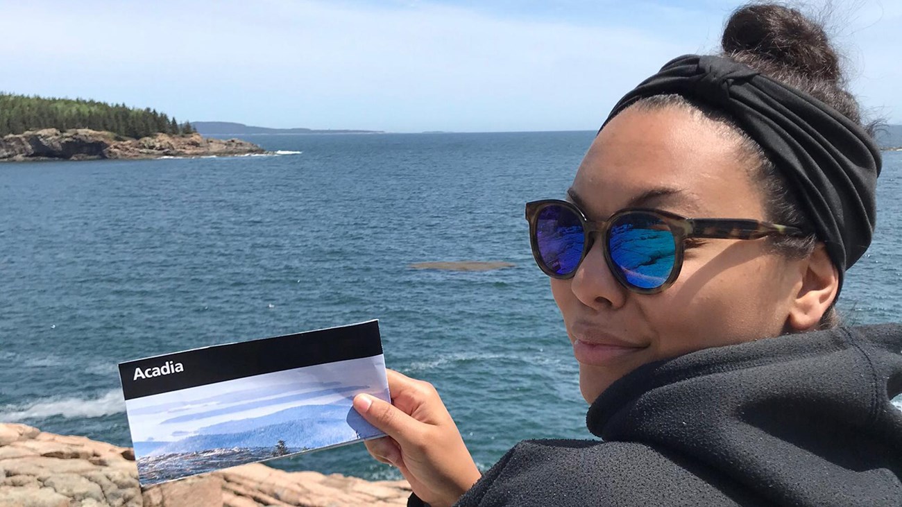Woman holding a park brochure stands along ocean coastline