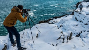 Photographer snaps photo of man standing in snow along coastline