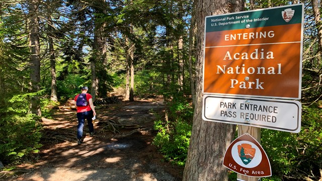 Visitor hikes on a trail past a park boundary and entry pass sign