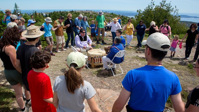 Group holding hands gathered around two indigenous people playing drums