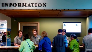 Three rangers talk to people at a desk under a sign reading "Information"