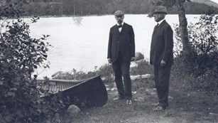 Two men with a boat stand beside a lake