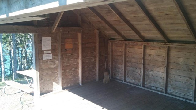 A wooden lean-to shelter with a broom in the far corner