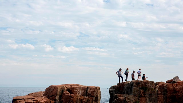 Five people on rock cliff near ocean