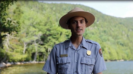 Park ranger wearing a green and grey uniform standing in front of a camera