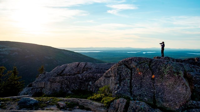 A person standing on granite taking photographs of the landscape