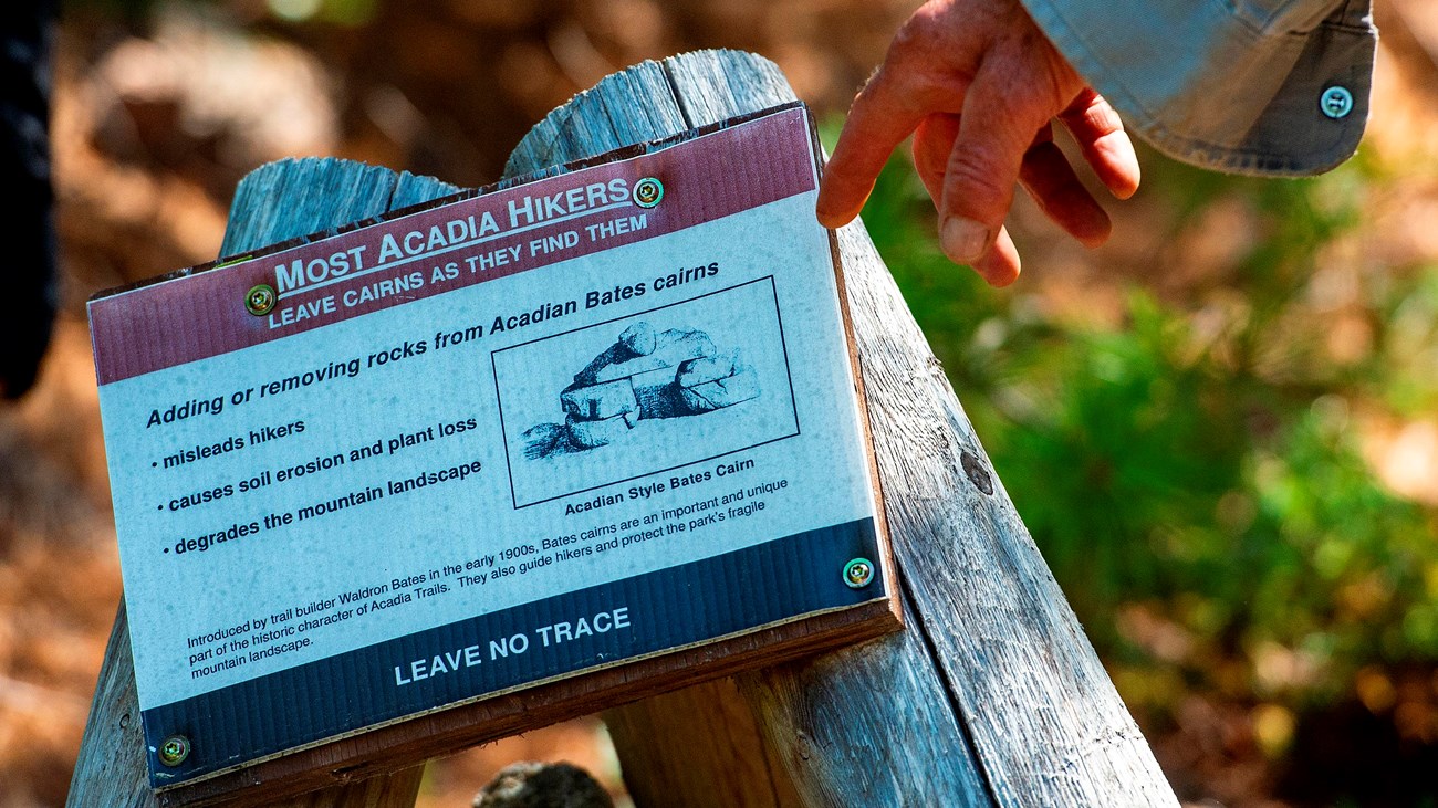 A person points to an informational sign on a wooden tripod