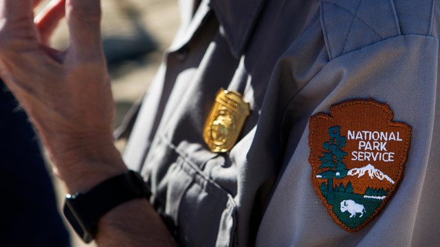 A grey uniform shirt with a gold badge and arrowhead patch