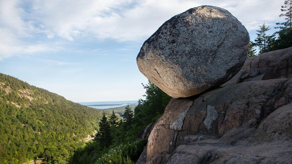 a large boulder perches on the edge of a mountain cliff