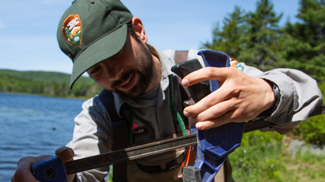 a ranger holding a turtle in front of a lake
