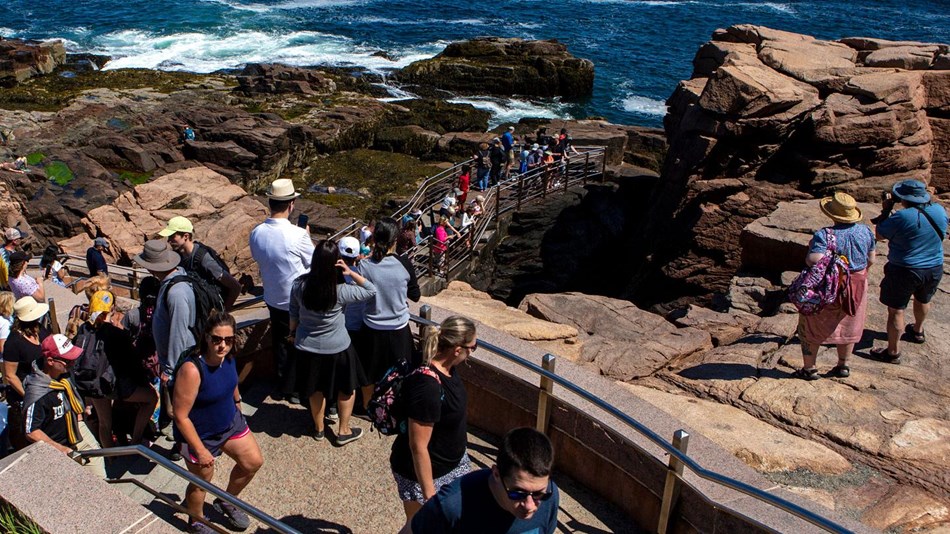 crowds of people walk down the steps toward a rocky ocean cliff