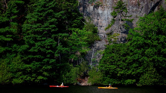 Kayakers paddle by cliffs along a lake