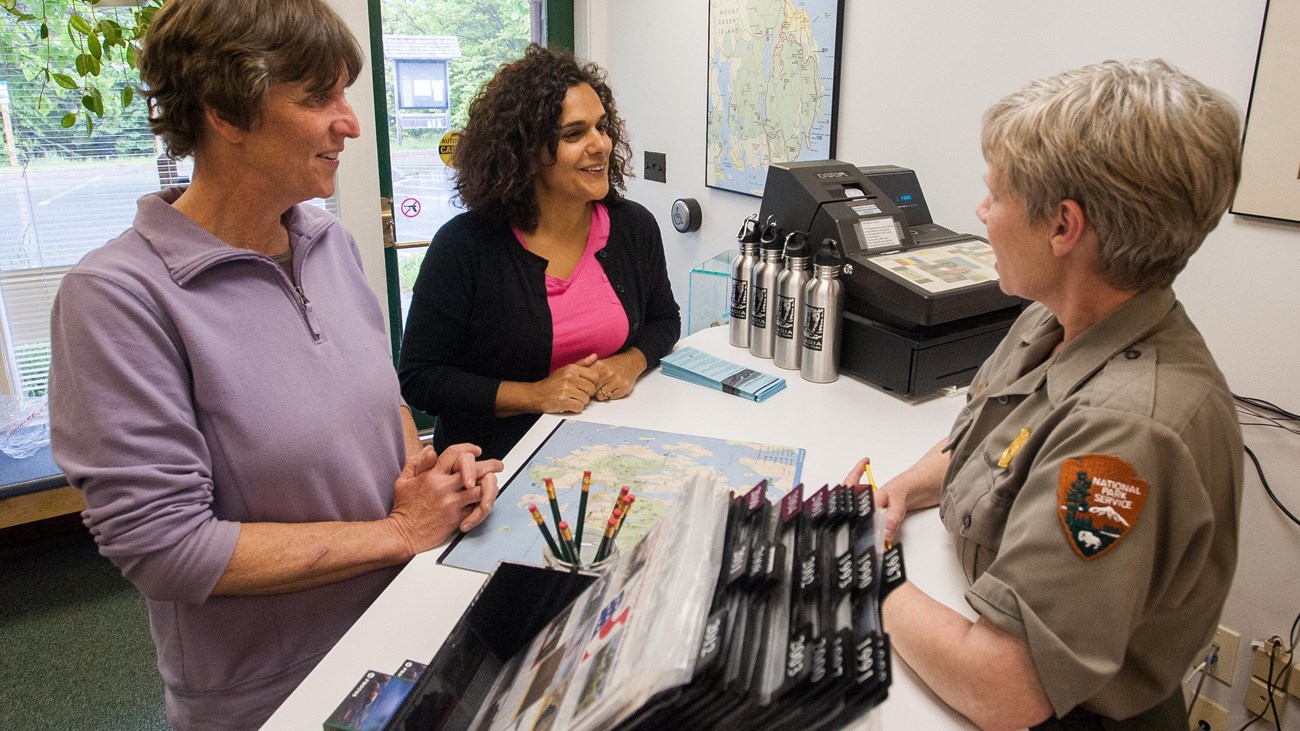 Two women speak with a uniformed ranger at an information desk