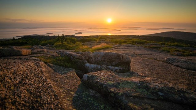 A mountain summit at sunset with a view of the ocean