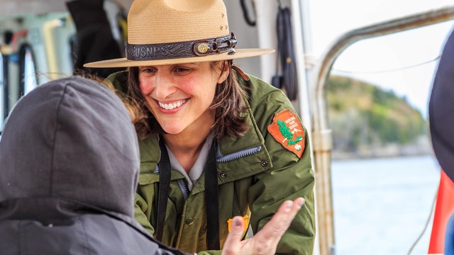 a ranger smiles at a hooded child on a boat