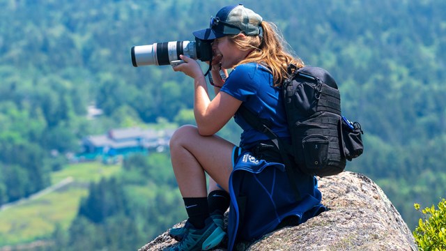 A photographer sits on a rock