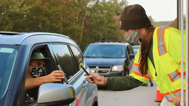 Ranger leans out of booth window to scan a device held by a driver of a vehicle.