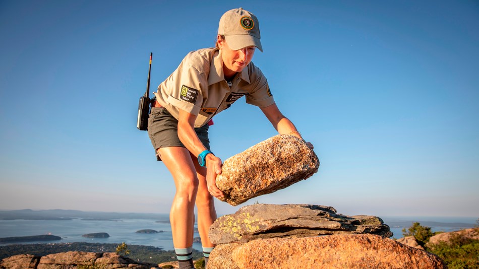 Woman stacks a rock for a trail marking cairn on a mountainside