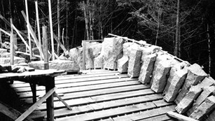 wooden supports in an arch with stone standing upright shows a bridge under construction