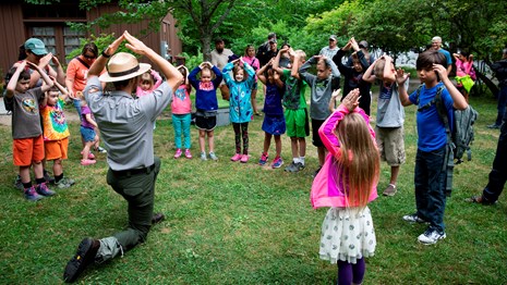 A park ranger and group of children in a circle with their hands up