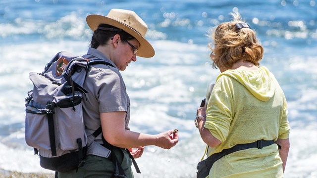 Ranger holding a small creature from a tide pool speaks with visitor