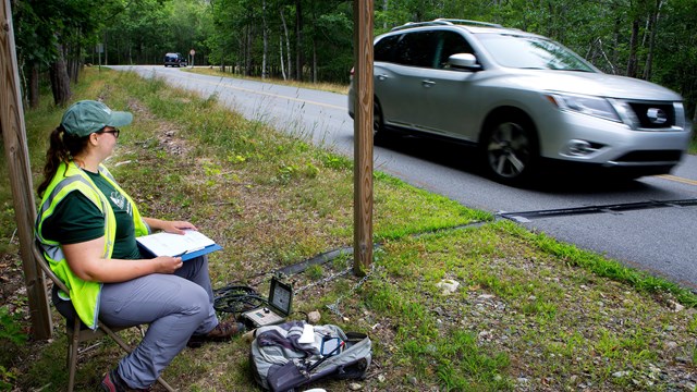 A technician seated next to road watches a car drive over a traffic monitor.