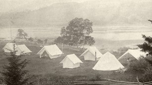 B&W photo of tents on a field in front of open water