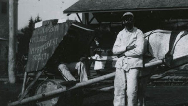 B&W photo of man in front of car bearing the words "Village Improvement Society"