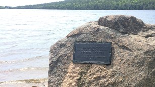 A bronze plaque on granite next to a lakeshore