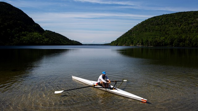 Person in a row boat pushing off a shoreline