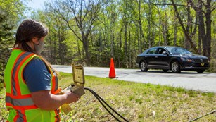 a person in a visibility vest reads a meter in front of a car on the road