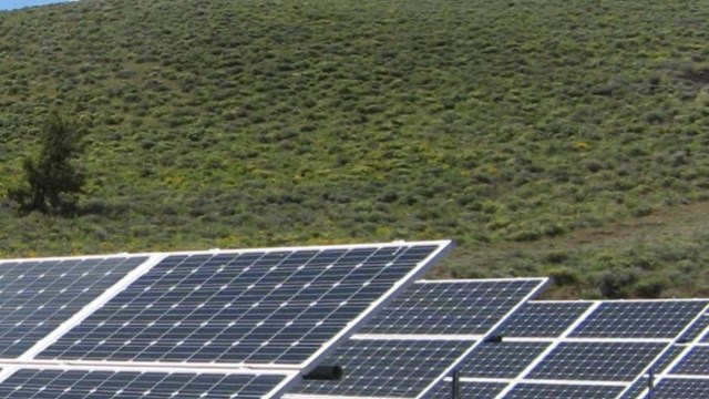 Solar panels in front of a hill with vegetation